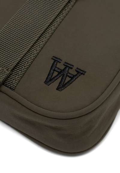Sac en tissu vert olive avec des bords arrondis, doté d'une anse texturée et d'un logo noir brodé dans le coin inférieur.