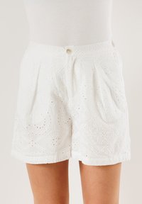 Pantaloni shorts bianchi in cotone con motivo a broderie anglaise, caratterizzati da tagli intricati, chiusura con bottone e design plissettato sul davanti.