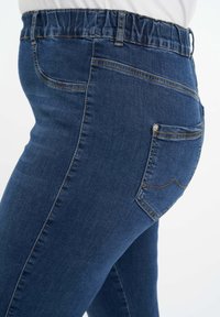 Denim leggings, joissa on joustava vyötärö, keskisininen väri, kapea malli. Takana on tasku, jossa on ompeluominaisuuksia, ja pinta on sileä.