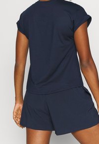 Marinblå träningsjacka med rullade korta ärmar, i kombination med matchande shorts. Tyget verkar mjukt och lätt, utformat för komfort.