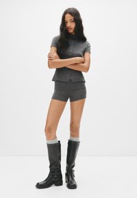 Grå kortærmet top med peplum-hulm og knaplukning, parret med grå shorts. Sorte knæhøje støvler med spænde-detaljer og grå sokker.