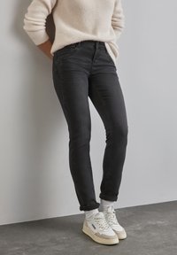 Svarta skinny jeans i denim med medelhög midja, subtila sömmar och avsmalnande passform, tillsammans med vita högtoppade sneakers och en texturerad tröja.