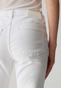 Jeans in denim bianco con un design aderente, dotati di due tasche posteriori e una trama liscia. Il girovita presenta un'etichetta in pelle con il logo.