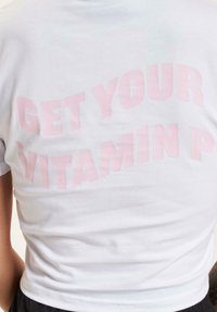Biele tričko s krátkym rukávom s veľkým svetloružovým textom "ZÍSKAJ SVOJU VITAMÍN P" na chrbte, s priliehavým strihom.