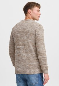 Lys brun strikket genser med en teksturert, melert design. Har rund hals og ribbestrikkede mansjetter og strikk. Bakvisning viser en avslappet passform.