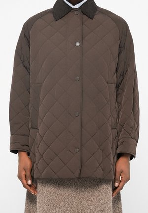 Veste matelassée marron avec des boutons-pression, un col foncé et des poches latérales portée sur une jupe en tricot beige, montrée des épaules jusqu’aux hanches.