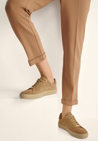 Zamszowe trampki w odcieniu tan z niskim profilem, okrąg�łym noskiem i sznurowanym zapięciem. Posiadają jasną podeszwę oraz minimalistyczne detale w przeszyciach.