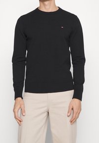 Schwarzer Langarm-Pullover mit Rundhalsausschnitt aus weicher Baumwolle, mit kleinem farbigem Logo auf der Brust und gerippten Bündchen sowie Saum.