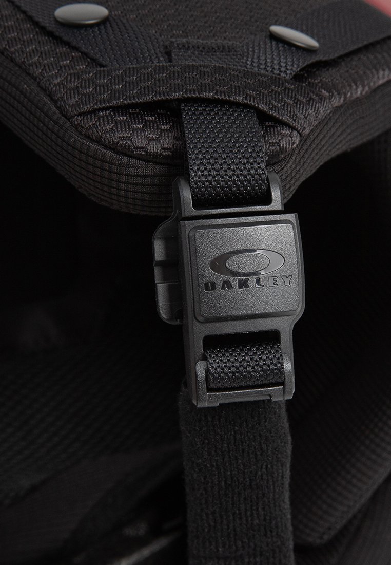 Schwarzer verstellbarer Gurt mit einer aus Plastik bestehenden Schnalle von Oakley, die an einem gepolsterten Stoff mit Nieten befestigt ist.