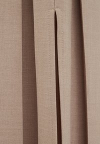 Tessuto beige chiaro con cuciture visibili, caratterizzato da uno spacco verticale e una superficie testurizzata, che enfatizza un'estetica strutturata e naturale.