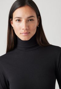 Pull en cachemire noir à col roulé avec un col haut, au design ajusté et à la texture lisse, comportant des manches longues et un subtil éclat.