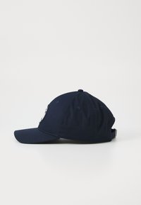 Marineblauwe baseballpet met een gebogen klep, verstelbare band en een embleem op de voorkant. Gemaakt van katoen en voorzien van ventilatie-openingen.