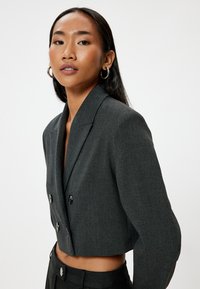Blazer corto de color gris oscuro con botones de doble botonadura, solapas marcadas y textura suave. Combinado con pantalones de talle alto a juego.