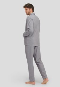 Conjunto de salón gris que incluye una chaqueta ajustada y pantalones a juego, confeccionado en tela texturada, con un corte relajado y un detalle mínimo.