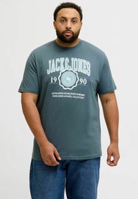 Hallide hallide T-särk lühikeste varrukatega. Esiküljel on valge "JACK & JONES" graafika, asutamisaasta "1990" ja ringikujuline disainielement.