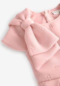 Rosa klänning med en rosett, strukturerad tyg med subtila präglingar och dragkedja i ryggen.