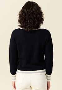 Pull marine avec col blanc et poignets côtelés. Texture douce, coupe ajustée et accents rayés en blanc et gris clair aux manches et à l'ourlet.