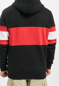 Sudadera con capucha que presenta un cuerpo negro con rayas horizontales rojas y blancas. Material de algodón con una textura suave y puños acanalados.