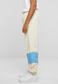 Pantaloni ușori, cu talie elastică, de culoare crem, cu un panou albastru la glezne. Prezintă o croială lejeră și manșete cu nervuri. Textură netedă.