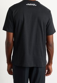 Camiseta de algodón negra con mangas cortas, que presenta un gráfico blanco "HAVE UNITE" en la parte superior de la espalda. Textura suave y corte relajado.