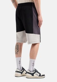 Pantaloni corti in materiale misto nero e grigio con vita elastica, caratterizzati da un fondo grigio chiaro. Indossati con calzini bianchi e sneakers nere.