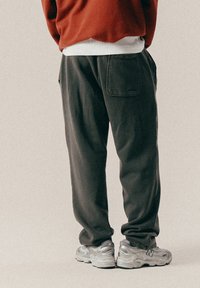 Mørkegr�ønne sweatpants med en afslappet pasform, der har baglommer og en glat overflade, parret med grå træningssko.