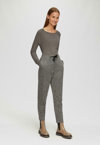 Graues Langarmoberteil kombiniert mit strukturierten schwarz-weißen gemusterten Hosen. Das Modell trägt braune Stiefel mit elastischen Seiteneinsätzen.