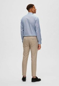 Lichtblauw overhemd met lange mouwen en knopen, beige tailleurbroek en zwarte schoenen. Het overhemd heeft een gladde textuur; de broek vertoont een subtiel patroon.