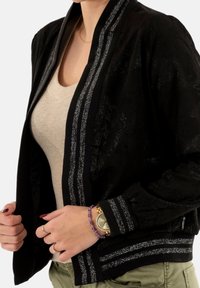 Veste bomber noire en tissu texturé, avec des accents rayés argentés sur les poignets et le col, présentant une coupe slim et des manches raglan.