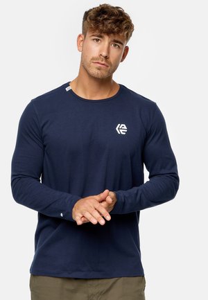 Camisa de manga larga en color navy, hecha de un tejido suave, con un escote redondo y un pequeño logotipo blanco en el lado izquierdo del pecho. Detalle de puño sencillo.