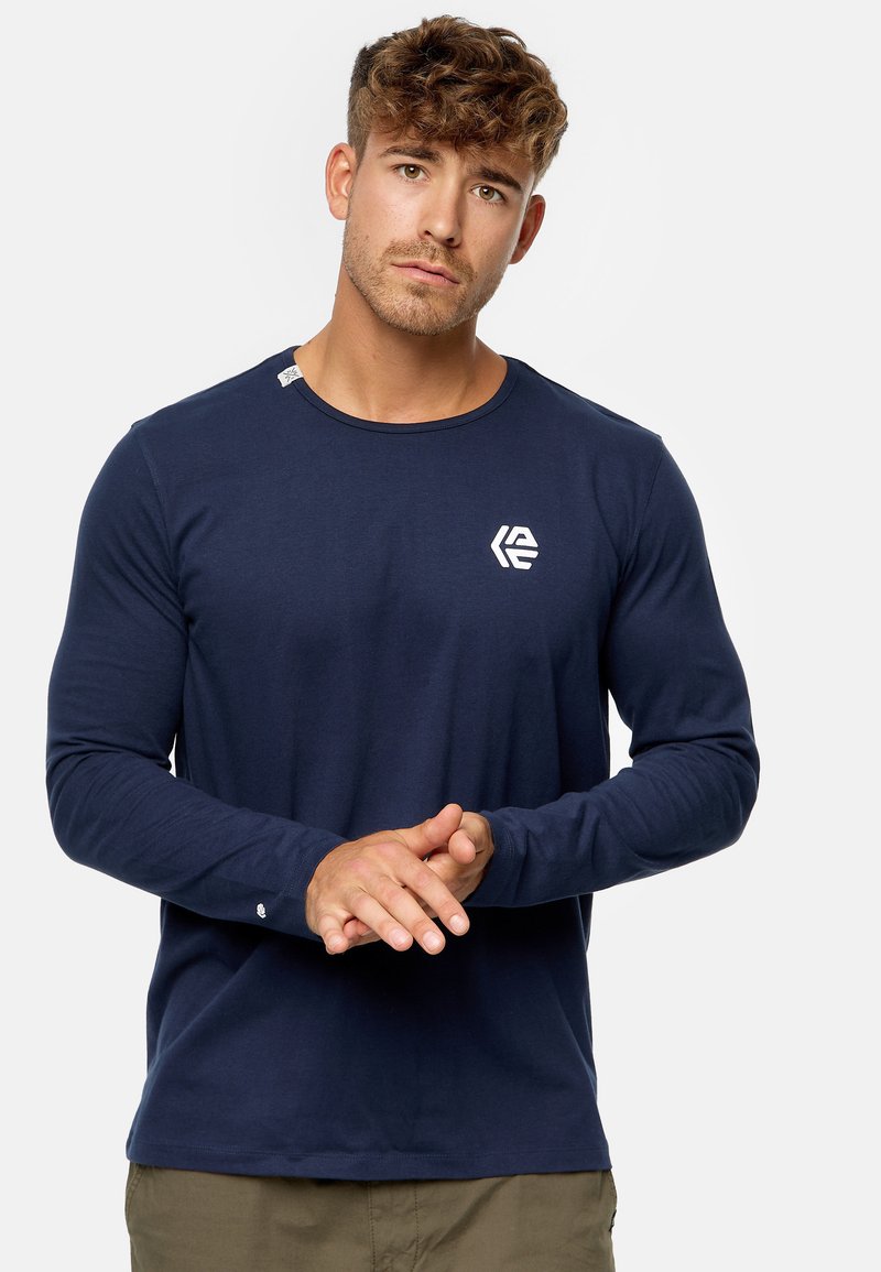 Camisa de manga larga en color navy, hecha de un tejido suave, con un escote redondo y un pequeño logotipo blanco en el lado izquierdo del pecho. Detalle de puño sencillo.