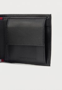 Zwarte leren portemonnee sectie met een muntzak flap en subtiel geperst Tommy Hilfiger logo op een witte achtergrond.