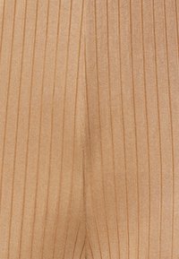 Leggings canelados numa tonalidade bege claro, com riscas verticais e um acabamento texturizado. O material parece elástico e suave.