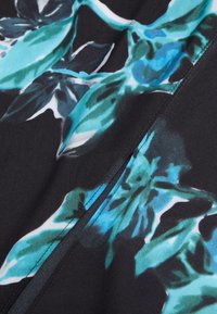 Svart tyg med ett blommönster i teal och vitt, med slät textur och en synlig söm på vänster sida.