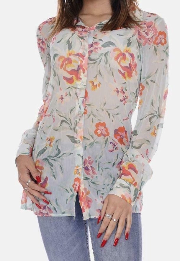 Blusa floreale con maniche lunghe, realizzata in un tessuto leggero e semi-trasparente. I colori includono motivi in rosa pastello, arancione e verde. Chiusura frontale con bottoni.