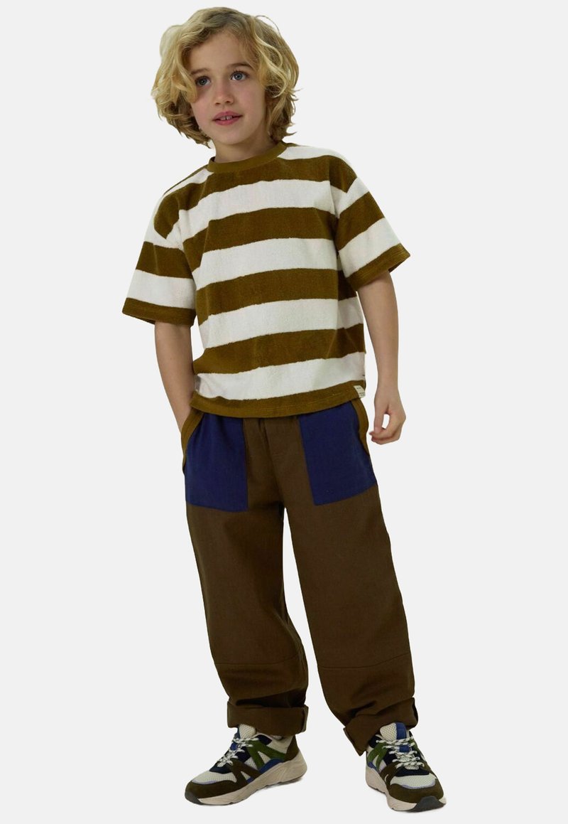 Gestreepte bruin- en witte shirt met korte mouwen, gecombineerd met losse bruine broeken met blauwe zakken en gelaagde schoenen. Zacht, textuur materiaal.