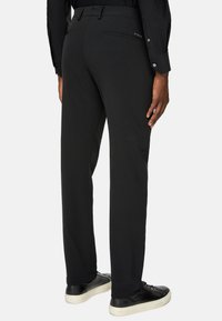 Svarta byxor i slätt tyg, med ett bälte, sidofickor och en bakficka med logodetalj, kombinerat med svarta sneakers.