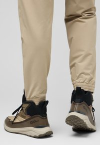 Le scarpe da trekking alte presentano un design beige e nero con una superficie texture, una suola robusta e un sistema di allacciatura per una vestibilità sicura.