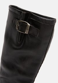 Black leather boot featuring a textured finish, a metal buckle accent, and a simple design with a slightly curved top opening.