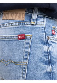 Világoskék farmernadrág hátzseb, vörös Big Star márkajelzésekkel és sárga varrással, sötét tengerészkék felsővel viselve.