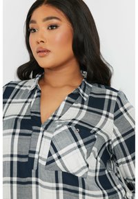 Camisa de cuadros en tonos azul marino y blanco, con cuello, bolsillo en el pecho y un corte relajado. Fabricada con un tejido ligero y suave al tacto.