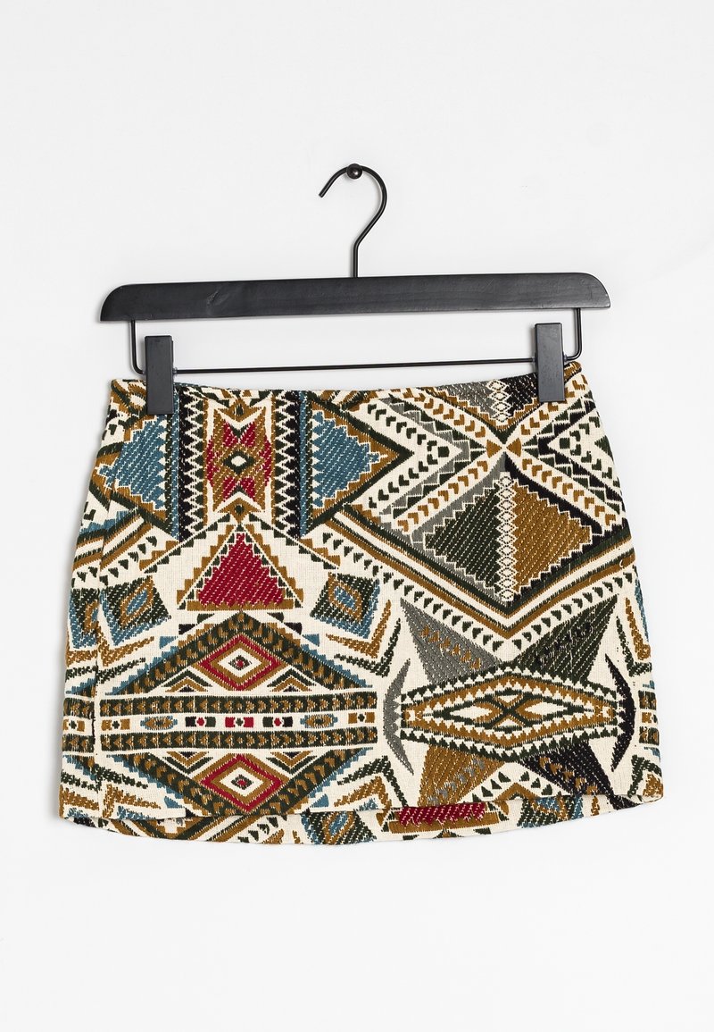Mini-jupe avec des motifs tribaux géométriques multicolores en rouge, bleu, marron, noir et blanc suspendue sur un cintre noir.
