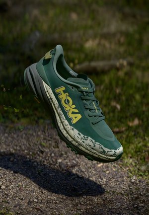Green running shoe with a textured upper, HOKA logo in yellow, and mottled light green midsole. Features a cushioned sole and traction pattern.