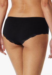 Schwarze Baumwollslips mit Spitzenrandverzierungen an den Kanten, die eine glatte Textur und einen klassischen Schnitt bieten.