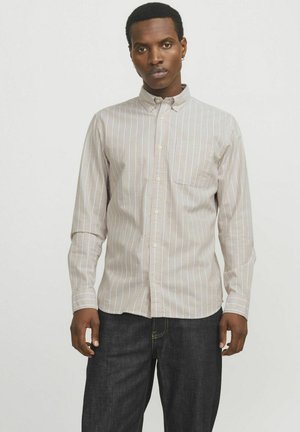 Camisa abotonada en rayas beige claro y blancas, de mangas largas, con un solo bolsillo en el pecho, de tela de algodón, combinada con jeans de mezclilla oscura.