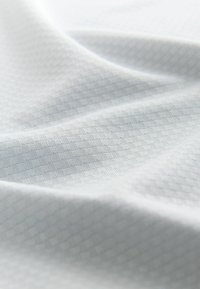 Texturiertes weißes Gewebe mit einem subtilen Diamantmuster, das eine weiche, glatte Oberfläche und einen leichten, flexiblen Fall zeigt.