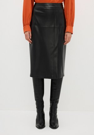 Jupe midi en cuir noir au design droit, avec des détails de coutures. Associée à des bottes noires jusqu'aux genoux et à un chemisier orange.