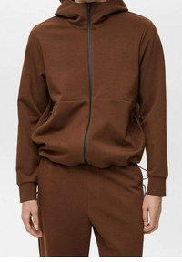 Felpa brown con zip realizzata in tessuto morbido, dotata di cappuccio, due tasche frontali e dettagli neri sulla zip. Vestibilità comoda con polsini a costine.