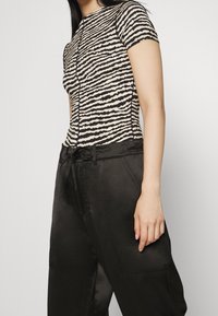 Tight-fitting topp med ett svart och beige randigt mönster, tillsammans med lösa svarta byxor med dragsko i midjan och sidofickor.