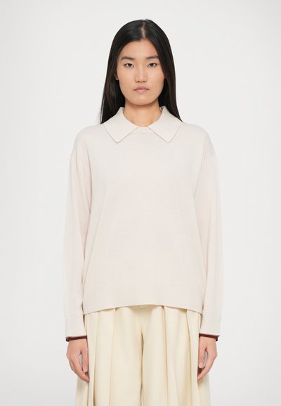 Suéter de punto color beige claro con un cuello ancho, hombros caídos y puños acanalados. Combinado con pantalones plisados color crema claro.